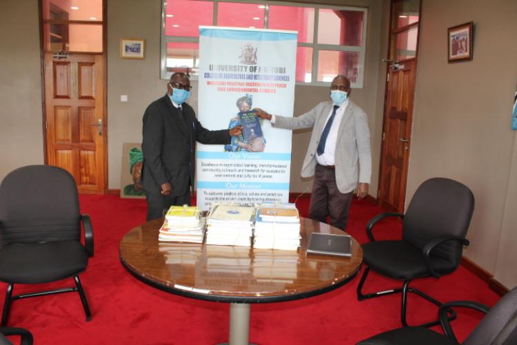 Prof. Nyamasyo (left) presents book donations to Prof. David Mungai, Director, Wangari Maathai Institute